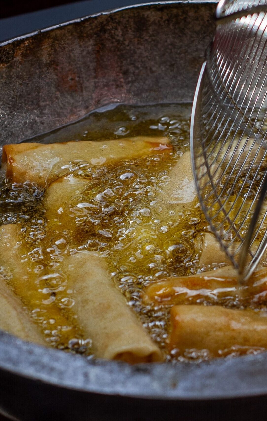 Close-up of spring rolls frying in hot oil, showcasing texture and heat bubbles.
