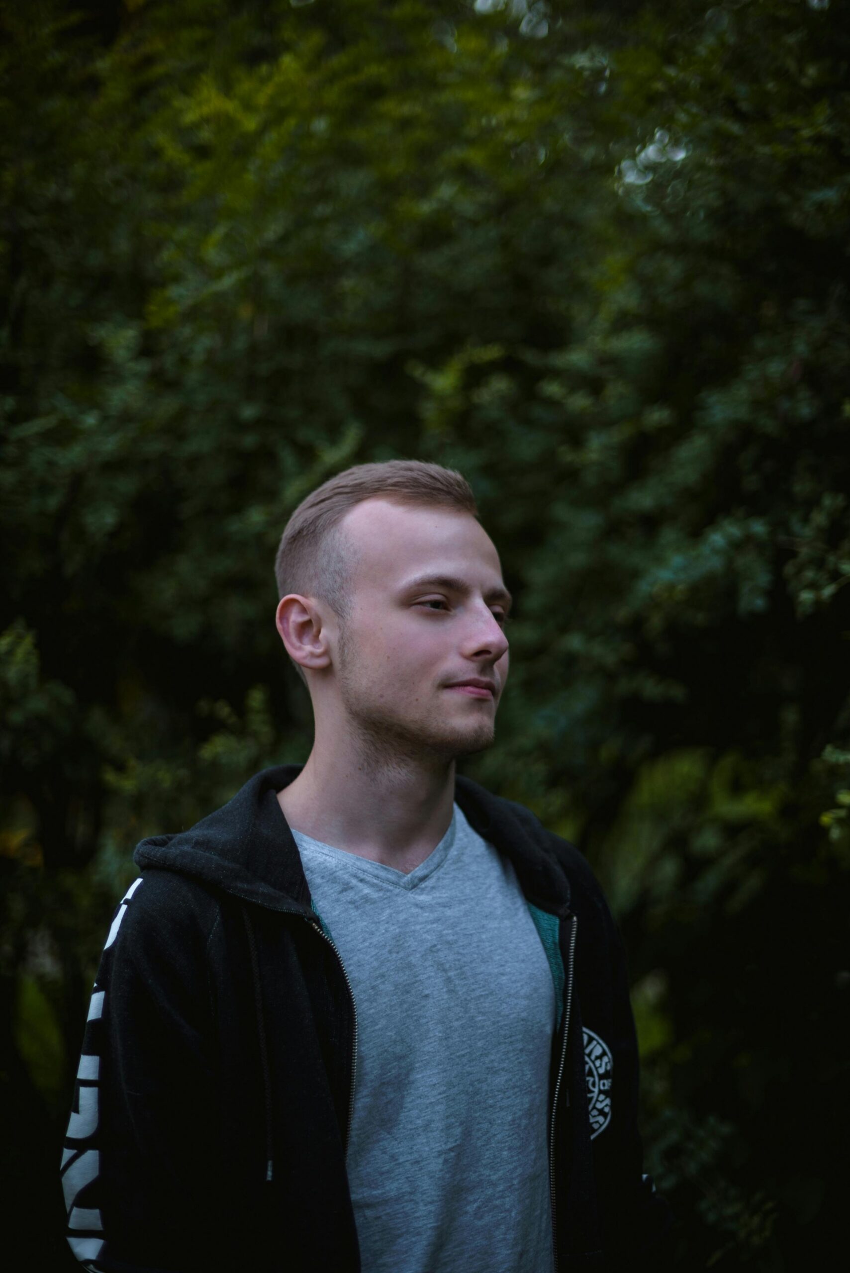 Profile portrait of a young man in a natural setting, surrounded by lush greenery.